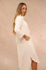 Vestido midi color crudo de estilo camisero, con cuello clásico, cierre frontal de botones, bolsillos laterales y mangas tres cuartos.