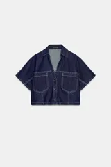 Camisa corta de denim de manga corta, con cuello solapa, escote en V y bolsillos delanteros de plastrón. Cuenta con costuras en contraste y cierre frontal con botones metálicos.