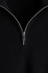 Buzo negro de tejido punto, con cuello alto y cierre metálico parcial frontal. Presenta un corte recto y mangas largas.
