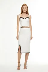 Falda midi color blanco con corte recto, abertura lateral y ribete negro en cintura, ruedo y abertura.