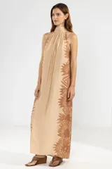 Vestido largo color beige con estampado floral marrón, corte recto, cuello halter y espalda descubierta.