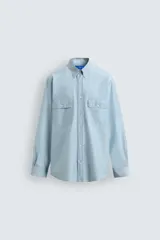 Camisa de corte relajado color celeste, confeccionada en mezcla de algodón y seda. Presenta cuello solapa, cierre frontal de botones, manga larga con puños abotonados y dos bolsillos de plastrón con solapa en el pecho.