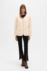 Chaqueta de pana color natural, con cuello a la base, cierre frontal y bolsillos delanteros tipo parche. Diseño holgado de manga larga.