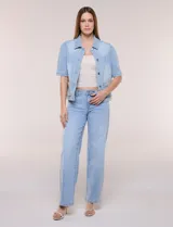 Camperita de denim color celeste con efecto lavado suave, cuello camisero clásico y cierre frontal de botones metálicos. Tiene mangas cortas con fruncido en los hombros, bolsillos delanteros bajos y costuras estructuradas.