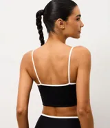 Top deportivo de microfibra con diseño alargado, escote recto y breteles finos. Presenta un detalle de bies contrastante en color blanco en el borde del escote y los breteles. Incluye copas internas para mayor soporte.