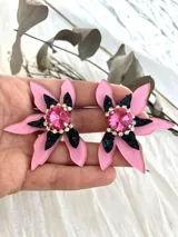 Par de aros con forma de flor de pétalos rosados con detalles en negro brillante y centro con gema facetada rosa rodeada de strass.