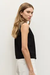 Blusa negra sin mangas, con cuello redondo y cierre frontal de botones ocultos. Presenta un aplique bordado con diseño abstracto en el lateral inferior.