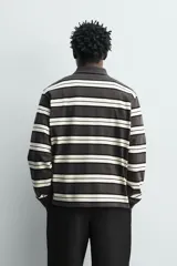 Polo de manga larga con diseño de rayas horizontales en tonos gris oscuro, negro y blanco marfil, cuello solapa y cierre frontal de botonadura oculta.