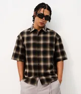 Camisa de corte boxy confeccionada en algodón, con diseño de cuadros escoceses y detalle de lettering bordado en el cuello. Presenta cuello camisero, mangas cortas y cierre frontal con botones.