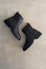 Botin de cuero vacuno color marrón, con taco bajo y suela track. Presenta una franja vertical negra en la parte trasera y cierre lateral.