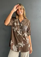Blusa de corte holgado color chocolate con estampado floral en tonos claros. Presenta cuello camisero con tapeta frontal decorada con lentejuelas y un bolsillo en el pecho también con aplique de lentejuelas. Posee mangas tres cuartos con detalle de trabilla para arremangar.