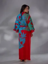 Kimono largo de algodón texturado con estampado vegetal en tonos rojo, azul y verde. Cuenta con mangas amplias, cinto independiente para ajustar a la cintura, bolsillos laterales y aberturas laterales en el dobladillo con detalles de flecos.