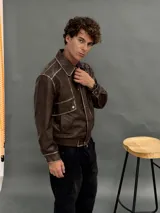 Campera estilo bomber de cuero sintético en color marrón con efecto desgastado. Presenta cuello camisero, cierre frontal con botones metálicos, bolsillos frontales con solapa y cintura elástica.