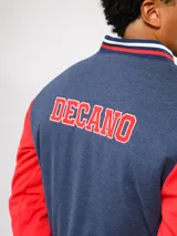 Campera bomber azul marino estilo retro, con cierre frontal de botones a presión, cuello, puños y ruedo con tejido acanalado tricolor. Presenta el logo de Umbro y el escudo del Club Nacional de Football bordados en el pecho, junto con el año 1899 y parches decorativos en las mangas.