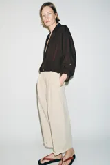 Blazer corto de color marrón oscuro, con cuello solapa, cierre frontal de botones y mangas largas con puños vueltos. Presenta un diseño con bajo elástico que le otorga una silueta ajustada en la cintura.