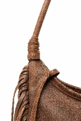 Cartera tipo hobo de cuero vacuno color tostado, con diseño amplio y flexible, decorada con un trenzado artesanal en el frente y largos flecos laterales. Cuenta con correa larga para llevar al hombro.
