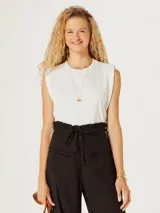 Camiseta sin mangas color blanco roto, con cuello redondo y hombros ligeramente caídos, de corte recto y ajustado al cuerpo.