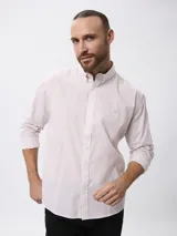 Camisa de manga larga con estampado de microcuadros en tonos azul y blanco. Presenta cuello clásico con botones, cierre frontal abotonado y detalle de logo bordado en el pecho.