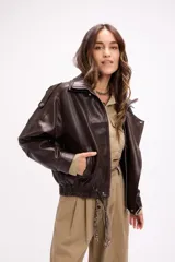 Campera estilo bomber oversize confeccionada en símil cuero negro con textura granulada. Presenta cuello alto con cierre frontal, hombreras marcadas, bolsillos laterales y cintura con elástico y cinto ajustable con hebilla metálica.