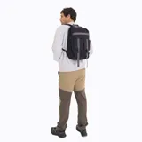 Mochila urbana Merrell de color negro con detalles en gris. Cuenta con un compartimento principal con cierre, un bolsillo frontal con solapa y correas ajustables con hebillas de plástico. Presenta una cinta horizontal decorativa y el logo de la marca en la parte superior.