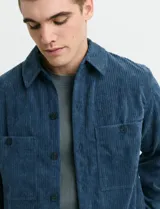 Sobrecamisa de pana color azul, con manga larga, cierre frontal de botones y dos bolsillos frontales con botón.