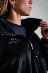 Buzo de plush color negro, con cuello alto y cierre frontal parcial, de manga larga con puños elásticos y diseño holgado.