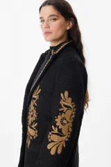 Blazer de textura suave en color crudo, con solapas clásicas y bordados florales en tonos tierra en el frente y las mangas. Presenta detalles de costura decorativa en los bordes de las solapas.