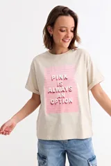 Remera de algodón color beige con cuello redondo y mangas cortas con dobladillo. Presenta un estampado frontal rectangular en color rosa con el texto en relieve 'PINK IS ALWAYS AN OPTION'.