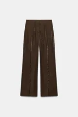Pantalón de tiro alto con pernera recta, confeccionado en tejido con acabado brillante y textura arrugada. Presenta bolsillos delanteros y cierre frontal con cremallera, botón interior y gancho.