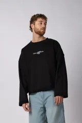 Buzo de cuello redondo confeccionado en tejido rústico con bordes al corte y costuras expuestas. Presenta un diseño boxy con estampado frontal y es reversible, permitiendo su uso por ambos lados.