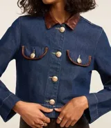 Campera de jean azul con cuello inglés de poliuretano color marrón. Cierre frontal con botones metálicos. Bolsillos de parche en el pecho con detalle de ribete de poliuretano marrón.