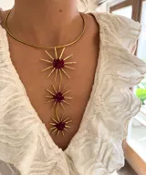 Gargantilla rígida dorada con tres dijes colgantes en forma de sol con centro de piedras rojas.