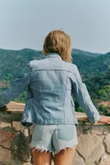Cazadora de denim de corte entallado, color celeste, con cuello subido, manga larga y cierre frontal con botones metálicos. Cuenta con bolsillos con solapa en el pecho y en la parte inferior delantera, además de presillas en los hombros.