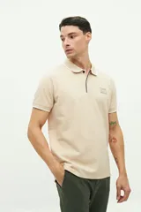 Chomba de piqué color beige con textura, cuello clásico con cierre de botones y detalles en contraste. Presenta mangas cortas con terminación en rib y logo estampado en el pecho.