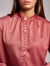 Blusa satinada color rosado con cuello mao, frunces en el escote y mangas largas. Cierre frontal con botones.