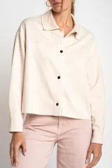 Camisa tipo sobrecamisa oversize color crudo, confeccionada en tejido de gamuza vegana con cierre frontal de botones metálicos y cuello clásico.