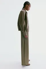 Pantalón de corte holgado en tejido fluido de satén verde militar, de piernas amplias, con bolsillos laterales discretos y cintura elástica con cordón ajustable y ribete de volado.
