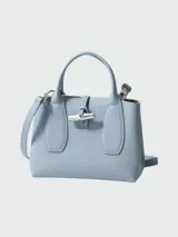 Cartera tipo tote de tamaño pequeño, confeccionada en cuero granulado color celeste. Presenta un diseño estructurado con asas cortas, cierre de solapa con el icónico broche de bambú metálico y correa ajustable para llevar cruzada.