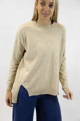 Buzo tejido de punto color beige melange, con cuello redondo acanalado, mangas largas de hombros caídos y aberturas laterales en el dobladillo asimétrico, más largo en la parte trasera.