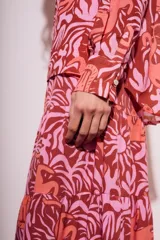 Blusa de poliéster con estampado de flores y animales en tonos rosa y marrón. Tiene cuello camisero, mangas largas y cierre frontal con lazo.