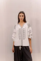 Blusa blanca con bordados en contraste de estilo bohemio, mangas amplias y diseño ligero.