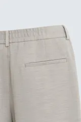 Pantalón de vestir color blanco hueso, de corte recto y tiro medio, con cintura elástica y cierre frontal de botón y cremallera. Presenta bolsillos frontales y bolsillos traseros de vivo.