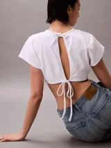 Remera cropped de algodón con corte boxy, cuello redondo y mangas cortas. Presenta un bajo redondeado en la parte delantera y un pequeño bordado de la marca en la manga.