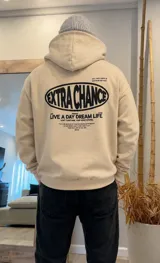 Canguro oversize color beige con capucha y estampado gráfico en la espalda con la frase 'Extra Chance' y texto motivacional en color negro.