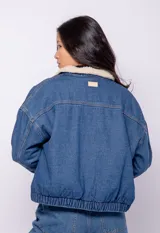 Campera de jean celeste con cuello y forro de corderito color crema, corte cuadrado, cierre frontal con botones metálicos, dos bolsillos de parche en el pecho y elástico en el ruedo.