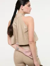 Top corto color beige, estilo halter con cuello alto y espalda descubierta. Confeccionado en eco cuero.