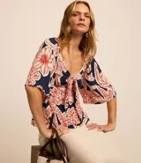 Blusa azul marino con estampado floral en tonos rojo y blanco, escote en pico con nudo y mangas cortas fruncidas.