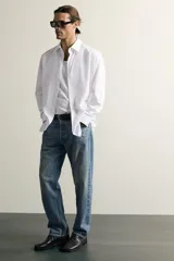 Jeans regular fit de mezclilla negra con efecto lavado, corte recto y tiro medio. Cuenta con diseño de cinco bolsillos y cierre frontal con cremallera y botón.