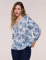 Blusa holgada de rayón y poliéster, marca Zac & Rachel, con estampado floral en tonos azules sobre fondo blanco. Posee escote en V con muesca central, mangas largas abullonadas con inserción de puntilla y puños elastizados.