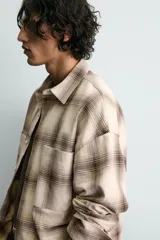 Camisa de algodón con cuello solapa, manga larga y dos bolsillos plastrón en el delantero. Presenta un patrón de cuadros en tonos beige y marrón oscuro.